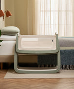 The SnuzPod 5 bedside baby crib with a lovely sage green wooden frame, next to an adult's bed in a beautifully decorated bedroom.