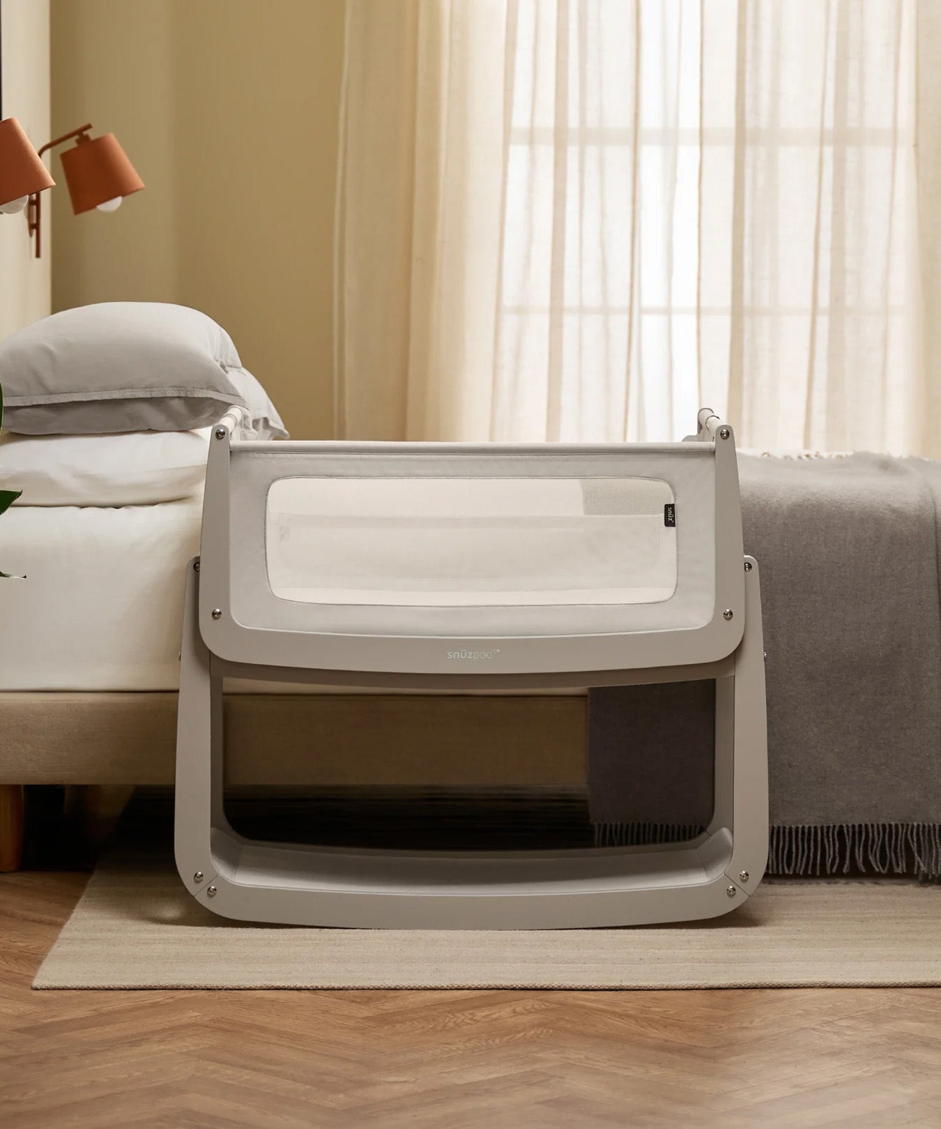 The SnuzPod 5 bedside baby crib with a lovely light grey wooden frame, next to an adult's bed in a beautifully decorated bedroom.