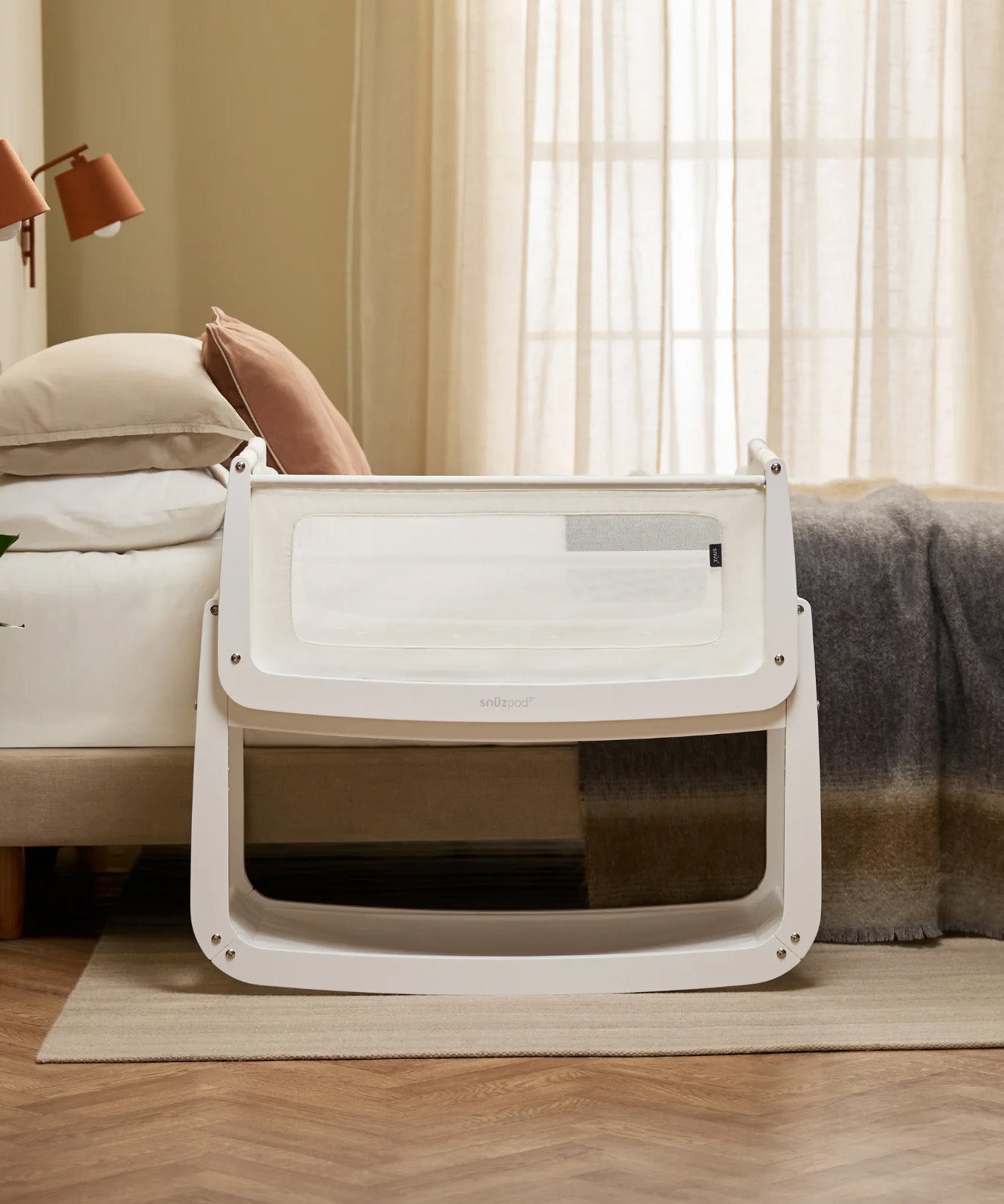The SnuzPod 5 bedside baby crib with a lovely white wooden frame, next to an adult's bed in a beautifully decorated bedroom.