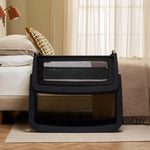 The SnuzPod 5 bedside baby crib with a lovely black wooden frame, next to an adult's bed in a beautifully decorated bedroom.