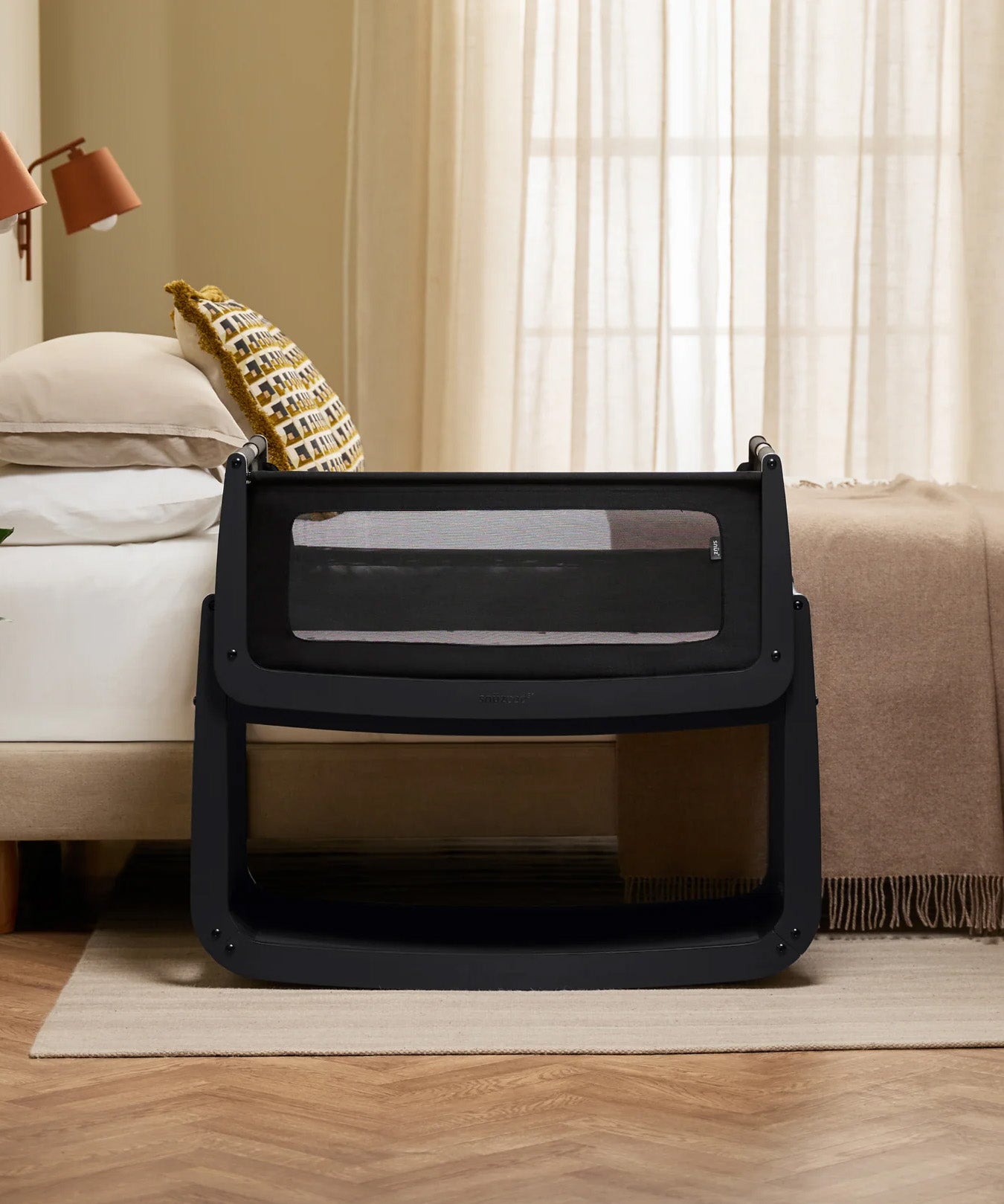 The SnuzPod 5 bedside baby crib with a lovely black wooden frame, next to an adult's bed in a beautifully decorated bedroom.
