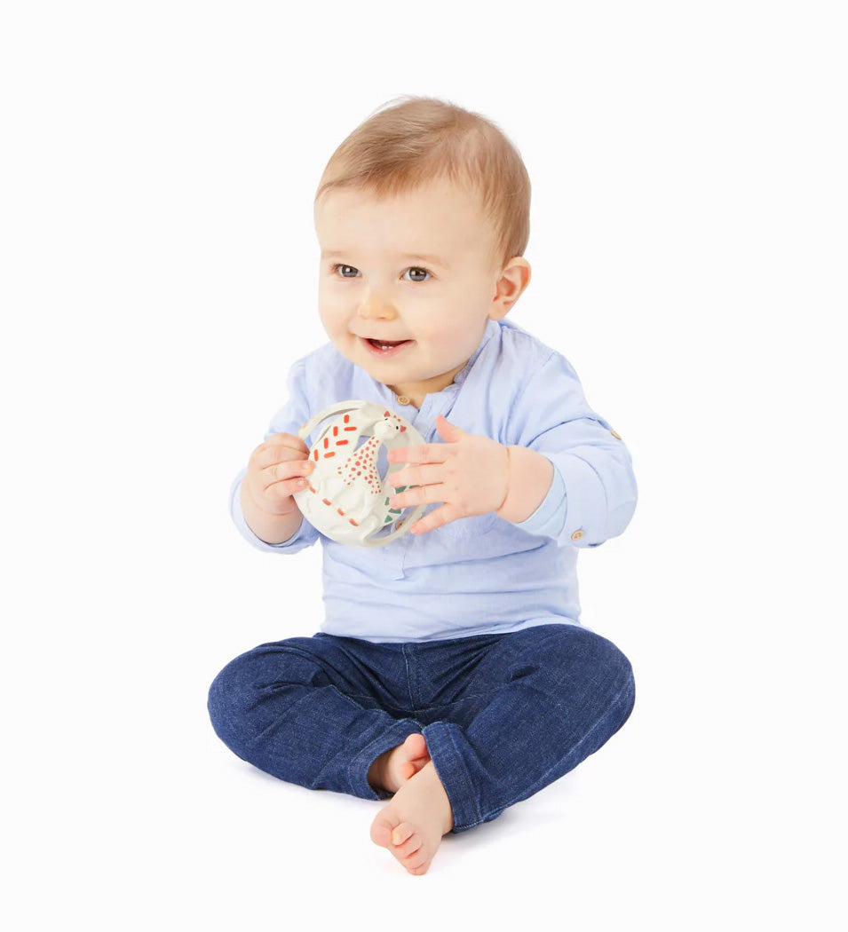 A baby playing with The Sophie the Giraffe natural Hevea rubber teething ball toy or babies, with non-toxic paints and textured elements. 