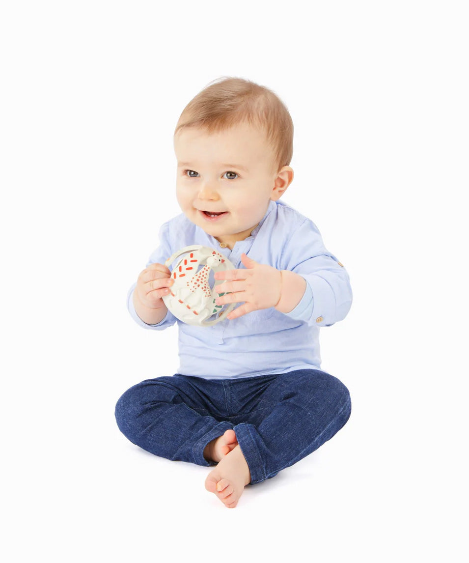 A baby playing with The Sophie the Giraffe natural Hevea rubber teething ball toy or babies, with non-toxic paints and textured elements. 