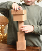 A close up of a child playing with the Bajo Square Pyramid Sensory Wooden Stacking Toy. The child is stacking the pieces in a random order. The set contains 5 wooden square and rectangular shaped blocks with a different coloured bases. Each blocks make a different sound when shaken. These heirloom quality toys by Bajo are part of a wide range of wooden toys available here at Babipur. 