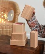 A close up of a child playing with the Bajo Square Pyramid Sensory Wooden Stacking Toy. The set contains 5 wooden square and rectangular shaped blocks with a different coloured bases. Each blocks make a different sound when shaken. These heirloom quality toys by Bajo are part of a wide range of wooden toys available here at Babipur. 