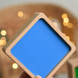 An adult's hand holding up the bottom blue piece from the Bajo Square Pyramid Sensory Wooden Stacking Toy. The set contains 5 wooden square and rectangular shaped blocks with a different coloured bases. Each blocks make a different sound when shaken. These heirloom quality toys by Bajo are part of a wide range of wooden toys available here at Babipur.  