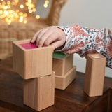 A close up of a child playing with the Bajo Square Pyramid Sensory Wooden Stacking Toy. The child is reaching for the pink cube block and placing it on the stack. The set contains 5 wooden square and rectangular shaped blocks with a different coloured bases. Each blocks make a different sound when shaken. These heirloom quality toys by Bajo are part of a wide range of wooden toys available here at Babipur. 