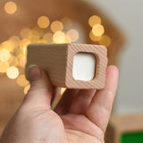 An adult's hand holding up the top piece from the Bajo Square Pyramid Sensory Wooden Stacking Toy. The set contains 5 wooden square and rectangular shaped blocks with a different coloured bases. Each blocks make a different sound when shaken. These heirloom quality toys by Bajo are part of a wide range of wooden toys available here at Babipur.  