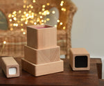Blocks from the Bajo Square Pyramid Sensory Wooden Stacking Toy placed on a small wooden table. The set contains 5 wooden square and rectangular shaped blocks with a different coloured bases. Each blocks make a different sound when shaken. These heirloom quality toys by Bajo are part of a wide range of wooden toys available here at Babipur. 