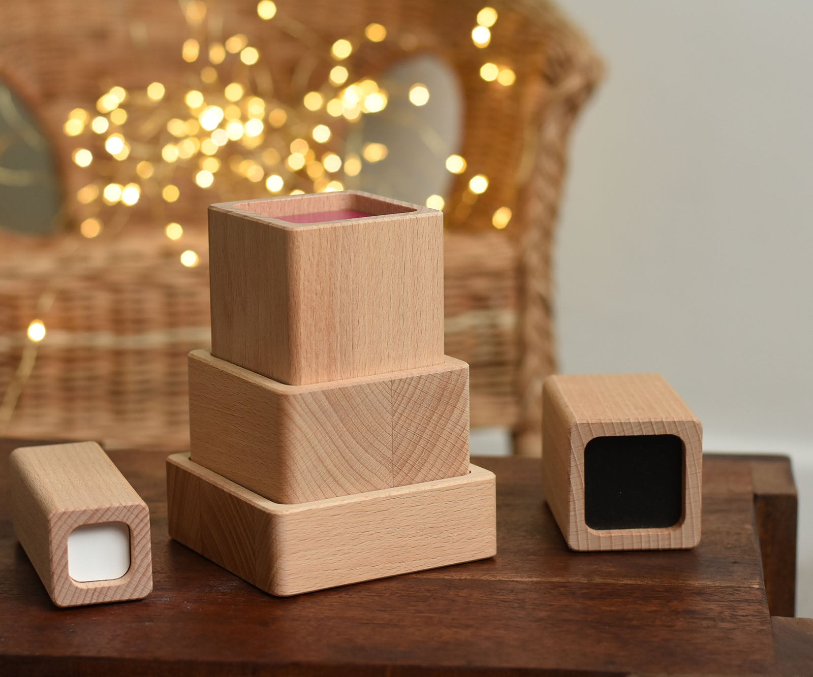 Blocks from the Bajo Square Pyramid Sensory Wooden Stacking Toy placed on a small wooden table. The set contains 5 wooden square and rectangular shaped blocks with a different coloured bases. Each blocks make a different sound when shaken. These heirloom quality toys by Bajo are part of a wide range of wooden toys available here at Babipur. 