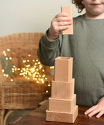 A close up of a child playing with the Bajo Square Pyramid Sensory Wooden Stacking Toy. The child has the tallest piece in their hand and they are about to place it on top of the stack. The set contains 5 wooden square and rectangular shaped blocks with a different coloured bases. Each blocks make a different sound when shaken. These heirloom quality toys by Bajo are part of a wide range of wooden toys available here at Babipur. 