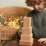 A close up of a child playing with the Bajo Square Pyramid Sensory Wooden Stacking Toy. The set contains 5 wooden square and rectangular shaped blocks with a different coloured bases. Each blocks make a different sound when shaken. These heirloom quality toys by Bajo are part of a wide range of wooden toys available here at Babipur. 