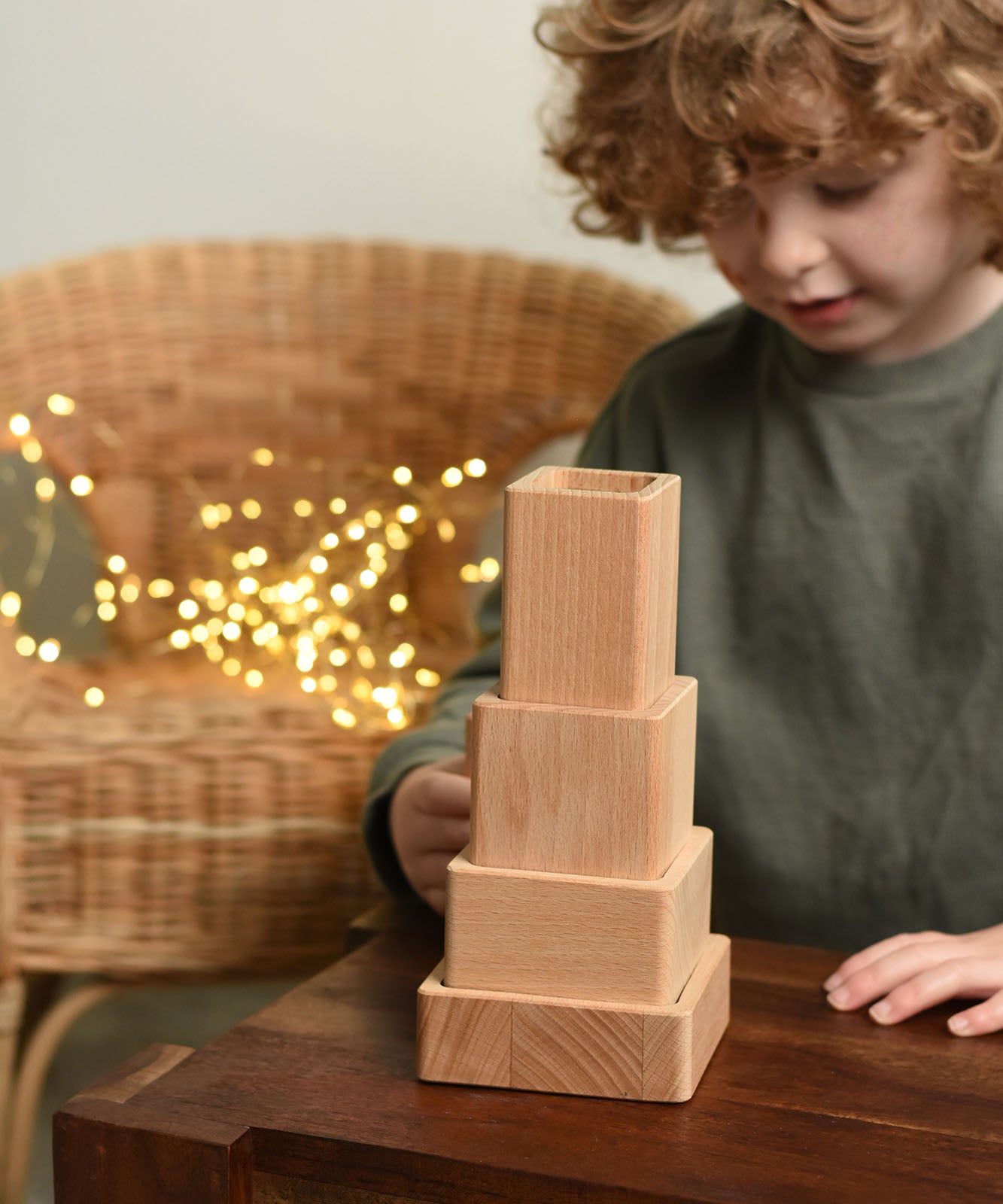 A close up of a child playing with the Bajo Square Pyramid Sensory Wooden Stacking Toy. The set contains 5 wooden square and rectangular shaped blocks with a different coloured bases. Each blocks make a different sound when shaken. These heirloom quality toys by Bajo are part of a wide range of wooden toys available here at Babipur. 