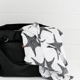A child in a baby bouncing chair looking at the XL Starfish Muslin cloth which is laid out on the side of a bath tub