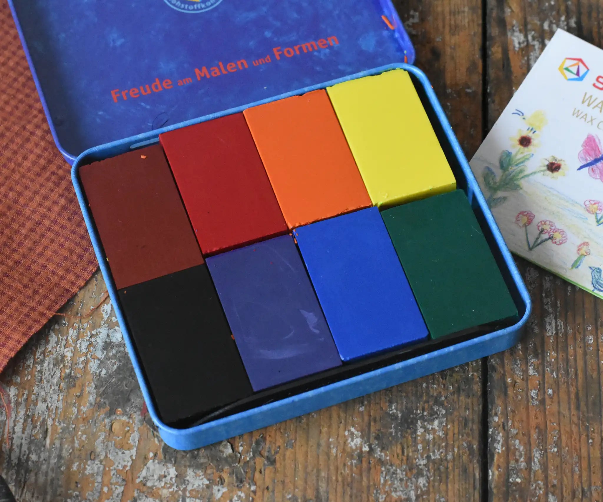 Stockmar 8 wax blocks in standard colours in a storage tin. Brown, red, orange, yellow, black, purple, blue and green.