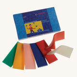 Stockmar Modelling Beeswax. 12 Sheets of coloured beeswax. The green, yellow, light pink, blue, red, orange and white modelling wax strips have been taken out of the box and placed in front of it. 