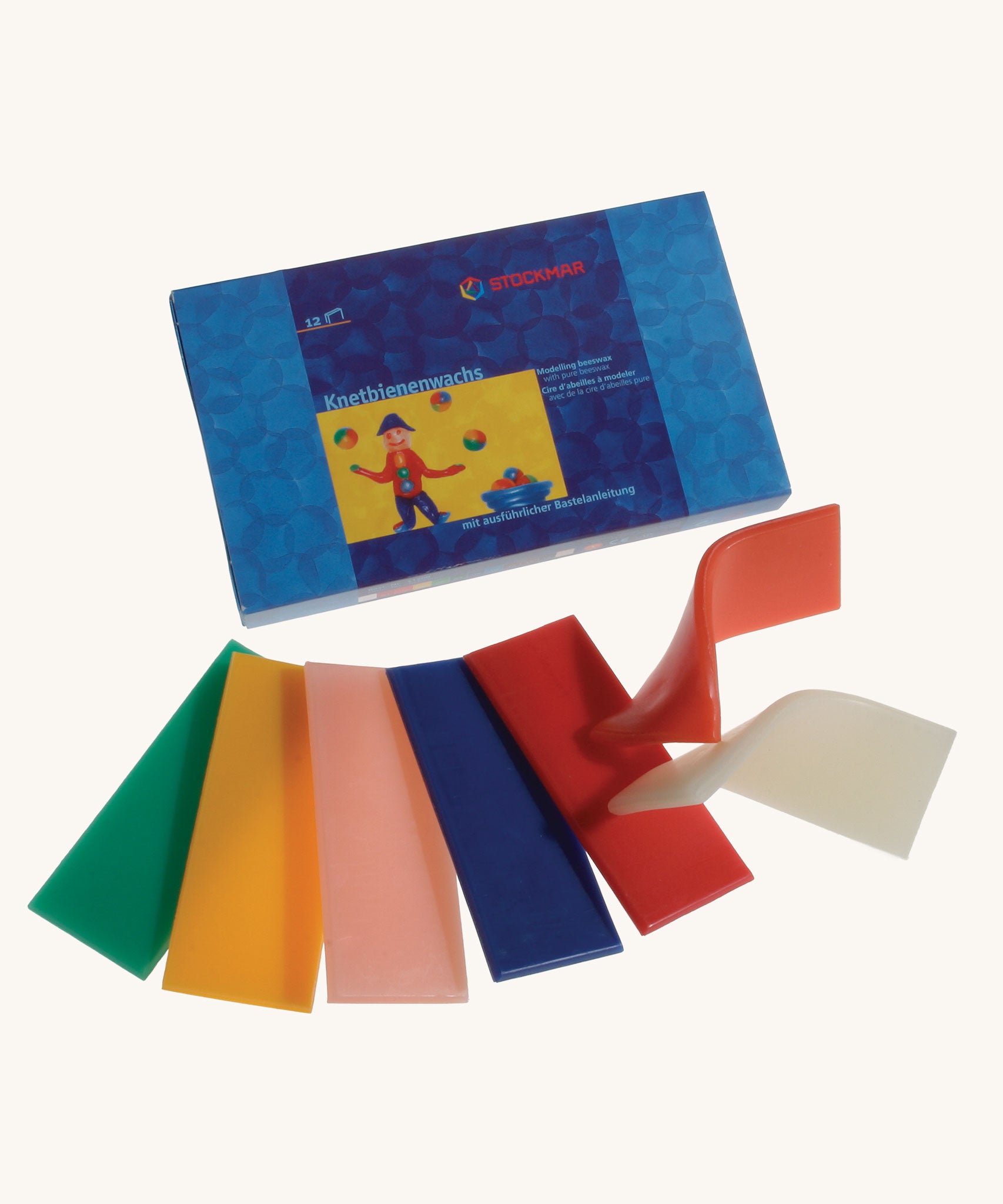 Stockmar Modelling Beeswax. 12 Sheets of coloured beeswax. The green, yellow, light pink, blue, red, orange and white modelling wax strips have been taken out of the box and placed in front of it. 