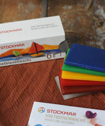 Stockmar modelling beeswax in a pack of 6 Sheets. White, brown, red, yellow green and blue sheets shown out of the cardboard box.