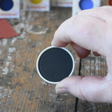 Stockmar black opaque watercolour replacement tablet in an adult's hand.