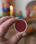Stockmar red opaque watercolour replacement tablet in an adult's hand.