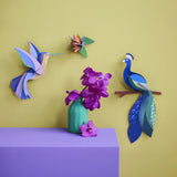A Studio Roof 3D paradise peacock bird perched on a branch craft kit displayed on a wall next to a hummingbird and bird model