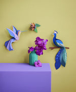 A Studio Roof 3D paradise peacock bird perched on a branch craft kit displayed on a wall next to a hummingbird and bird model
