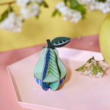 The Studio Roof 3D Pop Out Card Pear placed on a pink tray next to a yellow vase. This 3D pop out card DIY kit is part of Studio Roof's fruits collection which is available at Babipur. 