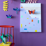 Stuio Roof insects mounted on a purple wall with a red chair in front and a plant and books