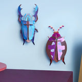 Studio Roof 3D cardboard azure stag beetle craft kit displayed on a wall next to a lumen pink beetle model