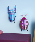 Studio Roof 3D cardboard azure stag beetle craft kit displayed on a wall next to a lumen pink beetle model