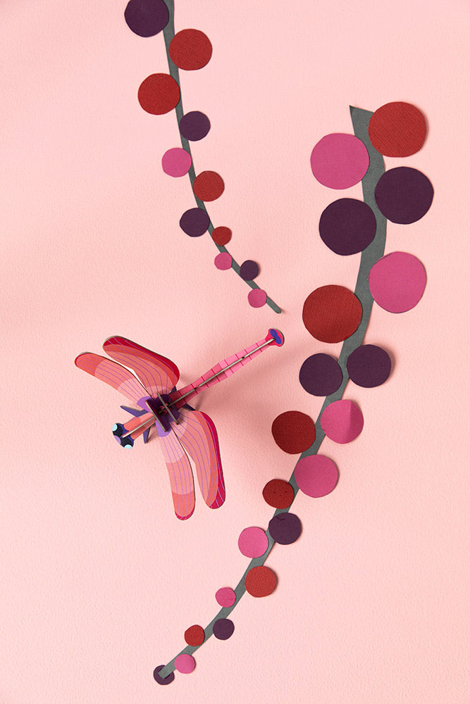Studio Roof Biodegradable recyclable cardboard ruby dragonfly on a light pink/peach background with paper pink and red plants/flowers