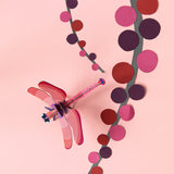Studio Roof Biodegradable recyclable cardboard ruby dragonfly on a light pink/peach background with paper pink and red plants/flowers