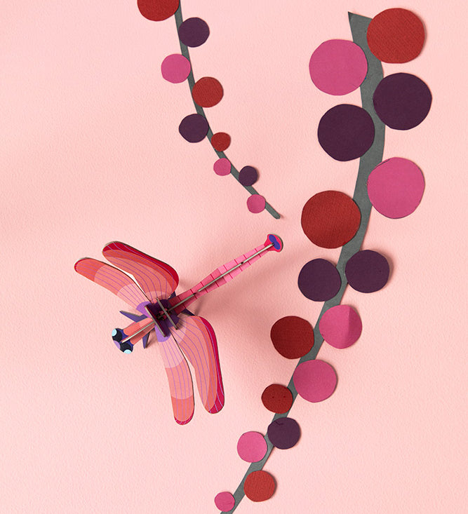 Studio Roof Biodegradable recyclable cardboard ruby dragonfly on a light pink/peach background with paper pink and red plants/flowers