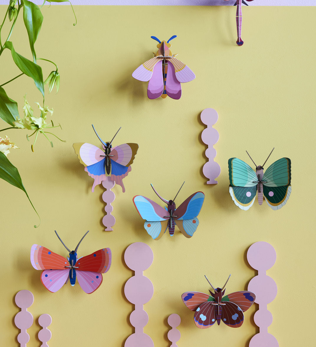 Collection of Studio Roof butterfly and insect decorations on a pastel yellow coloured wall with a pastel lilac border on the top