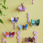 Collection of Studio Roof butterfly and insect decorations on a pastel yellow coloured wall with a pastel lilac border on the top