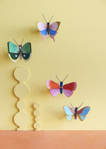 Collection of Studio Roof butterfly and insect decorations on a yellow pastel coloured wall