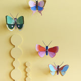 Collection of Studio Roof butterfly and insect decorations on a yellow pastel coloured wall