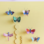 Collection of Studio Roof butterfly and insect decorations on a pastel yellow  coloured wall with a pastel lilac border on the top