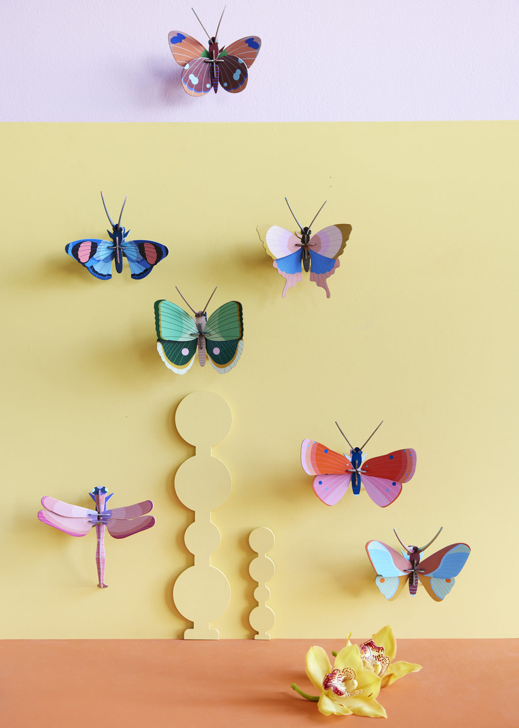 Collection of Studio Roof butterfly and insect decorations on a pastel yellow  coloured wall with a pastel lilac border on the top