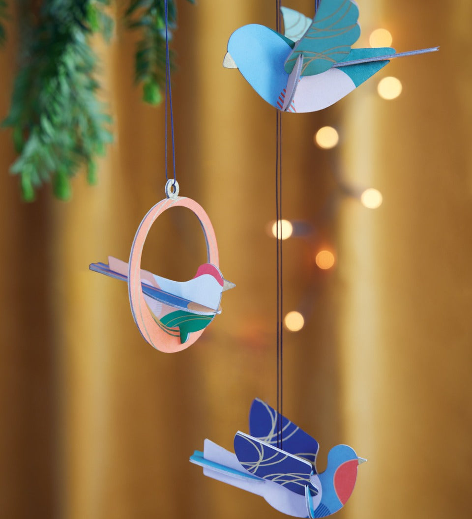 Close up of the Studio Roof plastic-free Calling Birds decorations hanging from a Christmas tree in front of an orange background