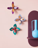 Studio Roof Lavender Cocktail craft flowers set hanging on a pink wall next to a blue vase