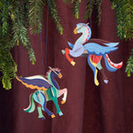 Studio Roof card craft Pegasus hanging decorations hanging from a Christmas tree in front of a deep red curtain