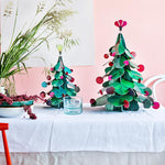 Studio Roof Large cardboard Christmas Tree & smaller cardboard Christmas tree on a table in front of a pink wall
