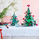 Studio Roof Large cardboard Christmas Tree & smaller cardboard Christmas tree on a table in front of a pink wall