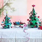 Studio Roof Large cardboard Christmas Tree & cardboard Squirrel Decor in the front and a smaller Christmas Tree with a cardboard peacock in a fruit bowl on a table
