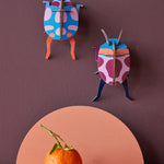 Studio Roof Coccinelle Couple Beetle decorations pictured hung up on a dark purple coloured wall