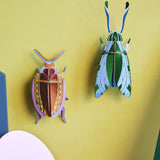 Studio Roof 3D cardboard Cuprum beetle craft kit displayed on a wall next to a jade grasshopper model