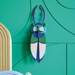 Studio roof slotting card antler beetle figure attached to a green patterned wall
