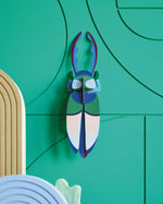 Studio roof slotting card antler beetle figure attached to a green patterned wall