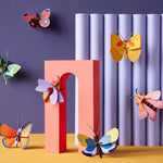 Studio roof slotting cardboard insect craft models attached to a red arch and some purple tubes in front of a dark purple wall